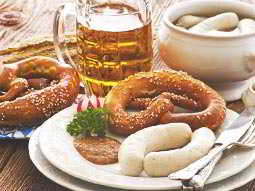 Various plates and bowls of pretzels and sausages surrounding a glass of beer