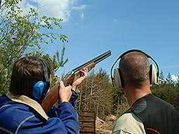 A man aiming with a shotgun whilst another man looks on