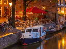 Two boats moored by the canal, with a seating area and some bikes parked 