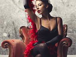 A woman with a feather boa around her, on a red, leather chair 