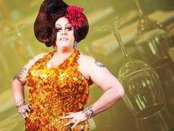 A drag queen with the outline of wine glasses behind her