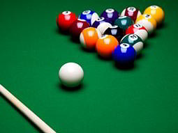 A 'racked' set of pool balls, a cue ball and a cue on a green pool table
