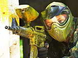 A man in camouflage and a mask, aiming with a paintball gun