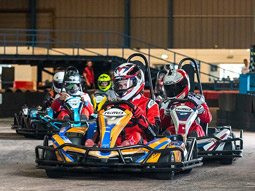A man driving a go kart around a corner at a quick pace, on an indoor track