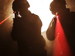 Two men aim guns emitting visible red laser beams past the camera