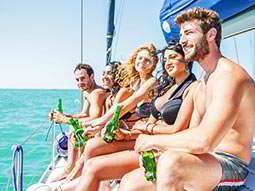 A group of people on the side of a boat relaxing with bottles of beer