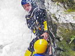 A man gorge scrambling and being splashed with water in a wetsuit and a helmet
