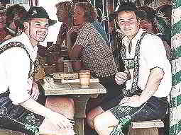 Two men wearing lederhosens sitting at a wooden table and chairs