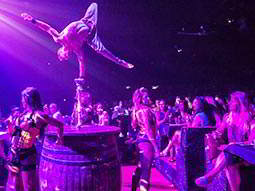 A man balancing on a barrel and performing to a crowd, to a backdrop of purple light