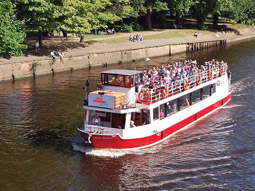 A red and white boat sailing on a river with a bridge in the background in York