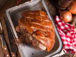 A large piece of cooked meat in a tray, with onions, a napkin and cutlery around it