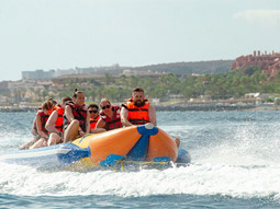 A line of people sat on a banana boat, being pulled by a white boat in the sea