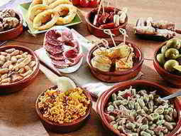 Various tapas dishes in red bowls, set out on a wooden table