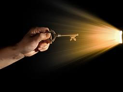 A man's hand holding a key to a light coming through a door