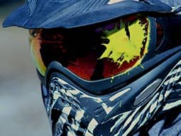 A man's paintball mask with paint splattered on the lens