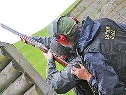 A man aiming with a shotgun with an instructor looking on behind him
