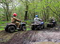 The backs of four men driving quad bikes through a muddy field