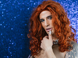 A drag queen in a glittery gold dress, with a red flower in her hair