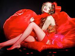 A woman reclining back on a red beanbag in a red burlesque outfit, whilst wearing a red trilby