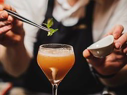 A female bartender placing a leaf on a yellow cocktail