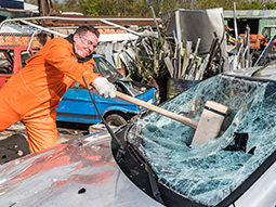 A man smashing a large hammer into the windshield of a car
