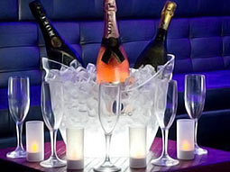 Bottles of alcohol in an ice bucket on a table, with wine glasses surrounding it