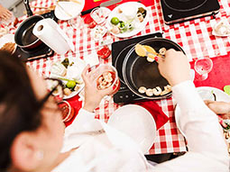 Someone putting some food into a saucepan, on a table with a gingham tablecloth