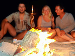A woman and two men sitting around a camp fire