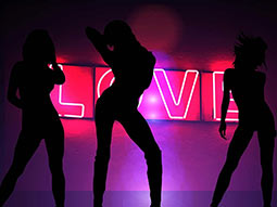 A silhouette of three women on a backdrop of the word 'love' in neon lights