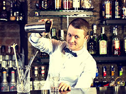 A man behind a bar pouring a drink into a glass from a cocktail shaker