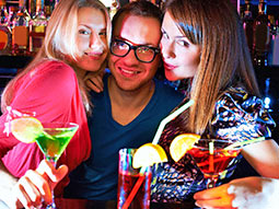 Two women and a man posing next to each other in a bar, with drinks in their hands