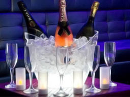 Three bottles of alcohol in an ice bucket on a table, with wine glasses around it