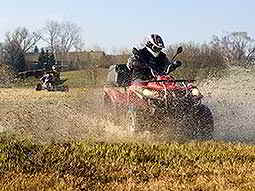 A quad bike being driven through a wet field, with another quad bike in the background