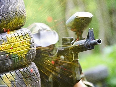 Man hiding beside tyres holding a paintball gun wearing camouflage