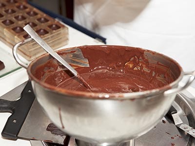 A metal mixing bowl full of melted chocolate with a metal spoon 