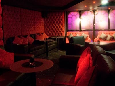 Image of a room with black leather sofas and chairs with red tufted fabric walls and red cushions and round wooden tables
