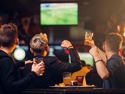 Image of three men standing watch football on a tv drinking beer