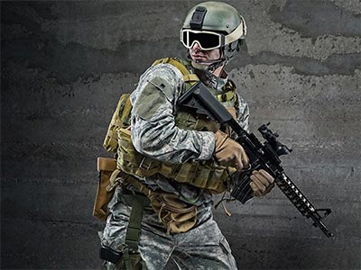 A man wearing army gear with goggles on holding a airsoft gun