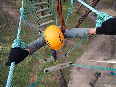 An aerial view of someone climbing high ropes, wearing a yellow helmet 
