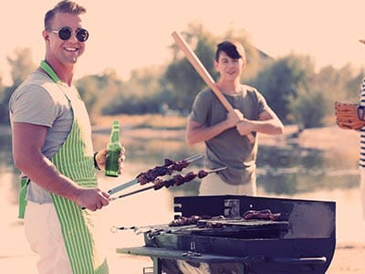 A man wearing sunglasses cooking on a bbq and a man holding a baseball bat