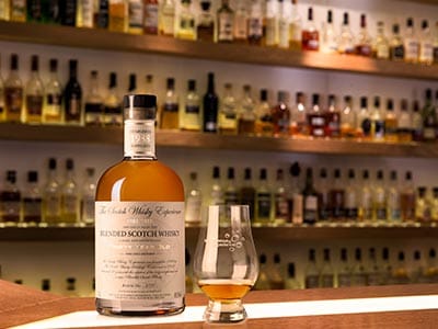 Image of a bottle of whiskey on wooden bar top with a whiskey glass and a whiskey display in the background
