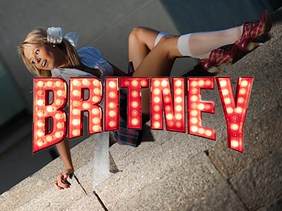 A girl lying on a pavement dressed in a school uniform and a Britney sign over