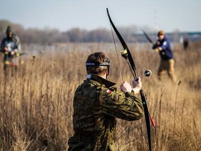 Image of men in a field with archery bows aiming to fire arrows at each other