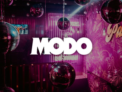 A room with lots of disco balls hanging and neon pink lighting with the Modo logo overlayed