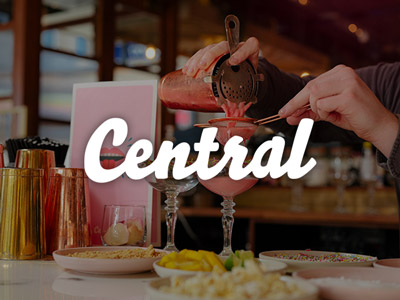 A pink cocktail being poured into a martini glass with the Central logo over the top