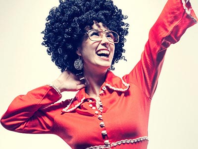 A woman in red flared bodysuit, black afro and sunglasses