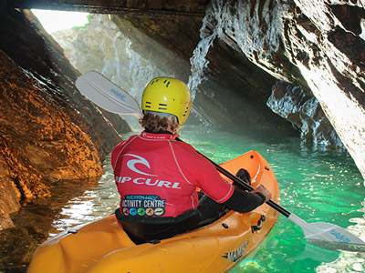 The back of someone kayaking through a small opening in a cave in Newquay