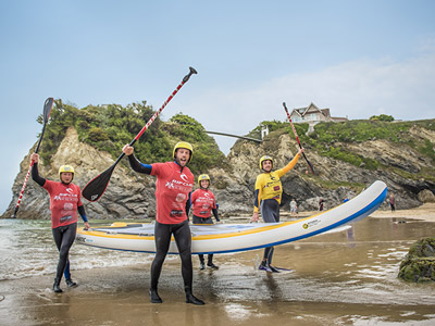 Four people on the beach holding ores and a SUP in Newquay