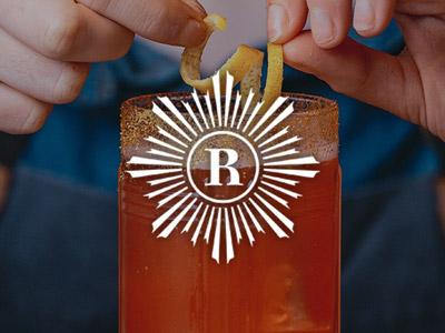 An orange coloured cocktail with glitter around the glass rim and a curl of lemon on top at Revolution