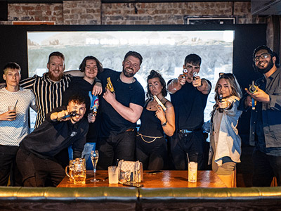 A group of people holding guns with drinks on a table in front of them at Point Blank